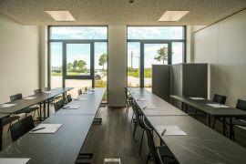 Seminarraum mit dunklen Tischen, Schreibunterlagen und Blick ins Grüne durch große Fenster.