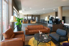 Hotellobby mit Sitzgruppen aus Leder und Stoff, Pflanzen und Selbstbedienungsbereich mit Kaffee.