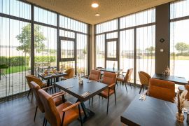 Restaurantbereich mit großen Fenstern, gedeckten Tischen und gepolsterten Stühlen in warmen Tönen.