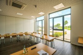 Tagungsraum mit natürlichem Licht, U-förmiger Bestuhlung und Blick ins Grüne durch Panoramafenster.