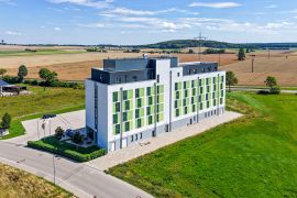 Modernes Hotelgebäude mit weiß-grüner Fassade in ruhiger Lage, umgeben von Feldern und Hügeln.