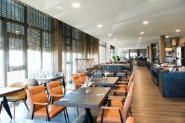 Großer Restaurantbereich mit Buffet, gedeckten Tischen und bodentiefen Fenstern mit Vorhängen.