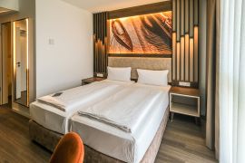 Doppelzimmer mit zwei Betten, moderner Wandbeleuchtung, Holzdetails und seitlichem Spiegel.
