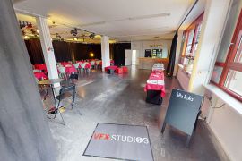 Großer Veranstaltungsraum mit VFX-Studios-Eingangsteppich, Buffetstrecke rechts, Sitzgruppen mit roten Decken und Bar im Hintergrund.