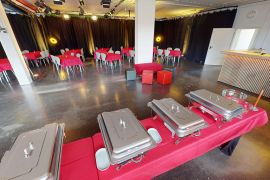 Veranstaltungsraum mit rot gedeckten Buffettischen im Vordergrund, Sitzgruppen im Hintergrund und Theke rechts an der Wand.