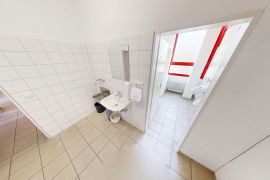 Heller, gefliester Sanitärbereich mit Waschbecken im Vordergrund und Blick in angrenzenden WC-Raum mit Toiletten.
